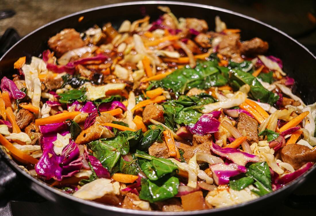 Vegetable Stir Fry in black Pan with beautiful greens and reds from leafy vegetables, carrots, tofu