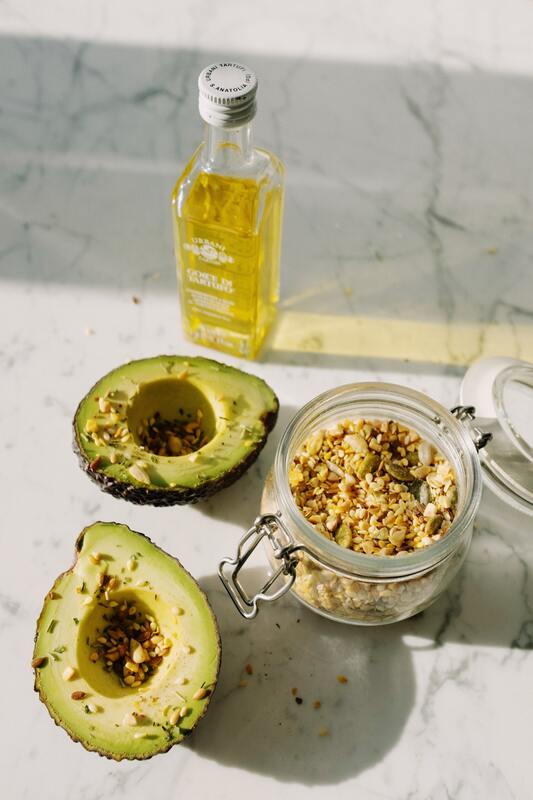 Avacados cut open with granola and a bottle of avacado oil on a granit coounter