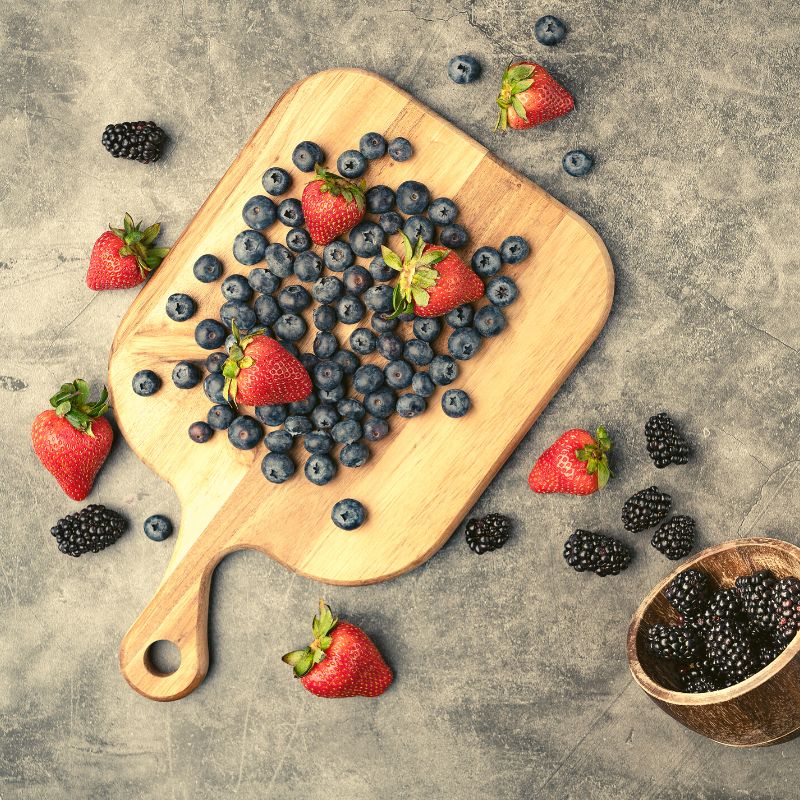 Image of berries on a wooden cutting board that has the name Twisted Paleo on the cutting board and other berries scattered from a bowl around the cutting board