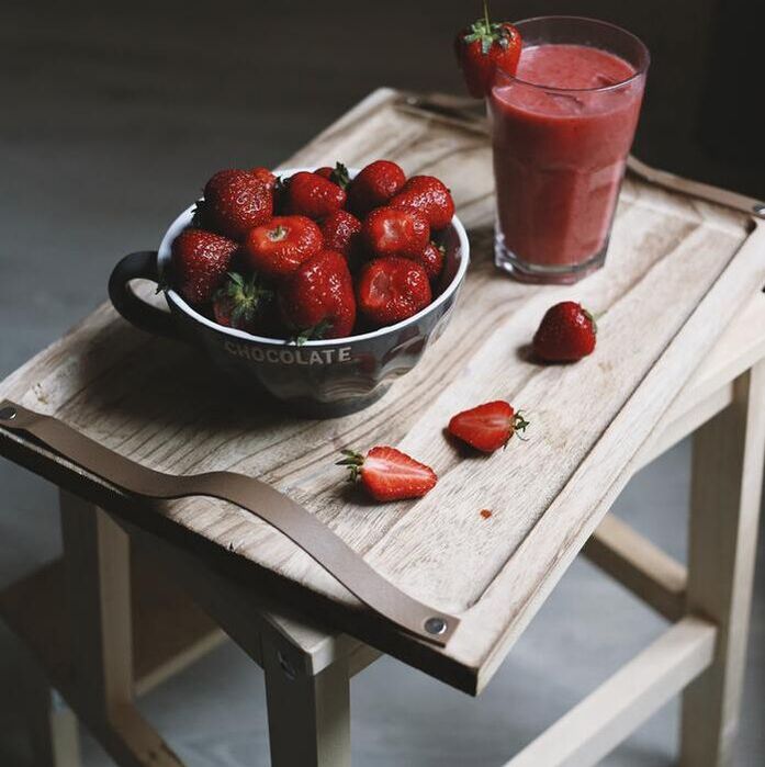rustic wooden tray that has a bowl full of strawberries, a cut in half strawberry and a strawberry smoothie